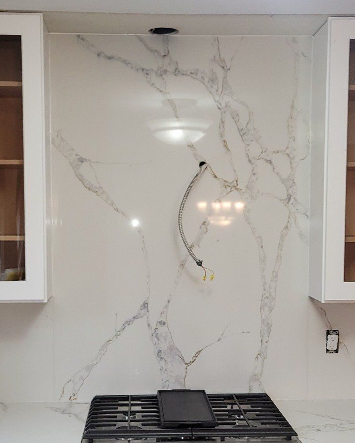 Kitchen with a full height backsplash: a veined white slab runs unbroken from the countertop up to the wall cabinets behind the range